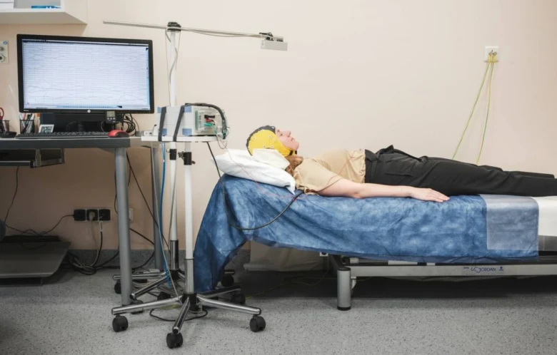 Osoba leží na lůžku s elektroencefalografickým čepem pro vyšetření mozku.