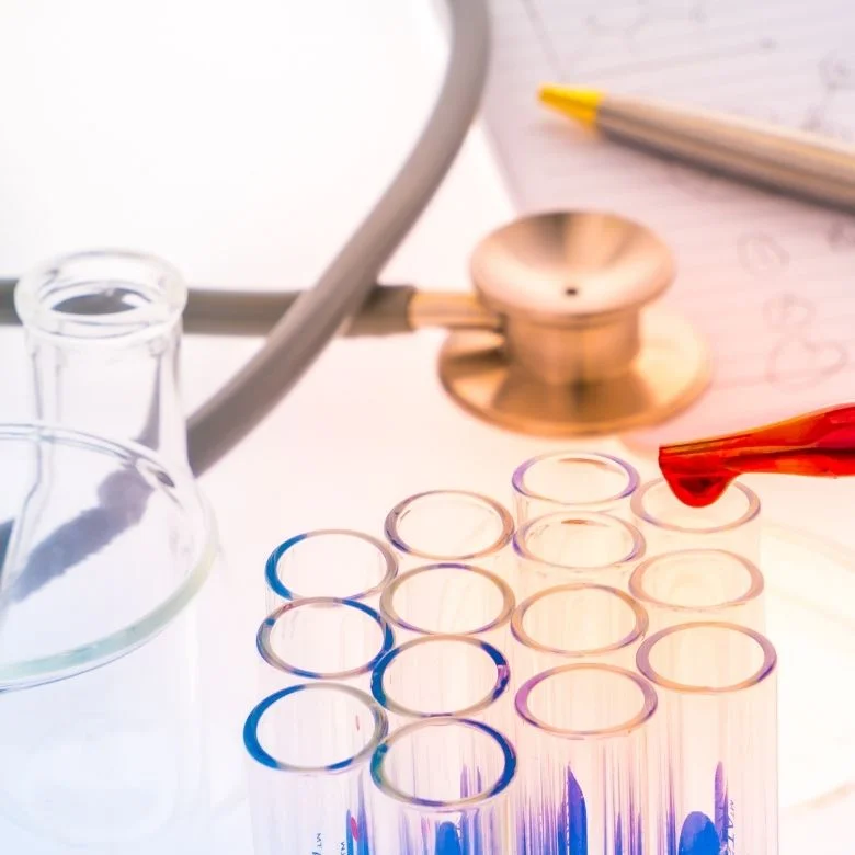 Laboratorní sklo s pipetou a fonendoskopem na bílém pozadí.