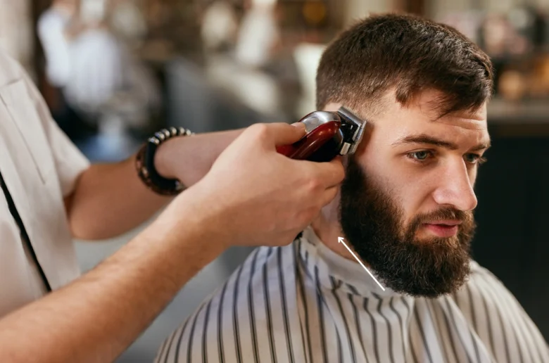 Barber oholí vousy na krku klienta pomocí strojku.