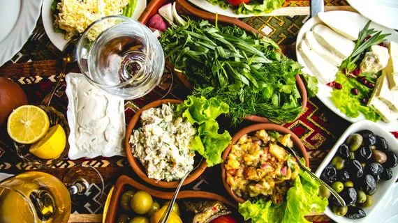 Stůl s mediterránskou kuchyní: zelenina, olive, sýr a víno.