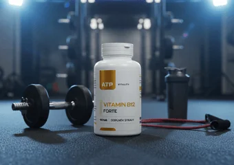 Bílá lahvička vitamínu B12 vedle činky v posilovně.